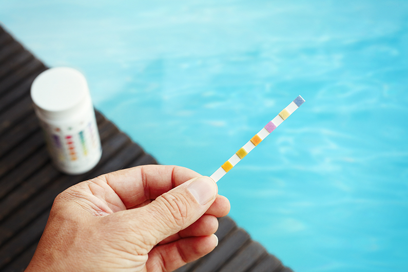 Main tenant une bande de test de la qualité de l'eau d'une piscine.