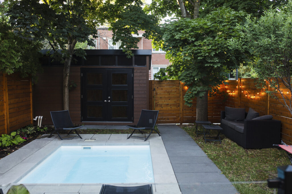 Petite poolhouse en bois dans un jardin au bord d'une piscine carrée.