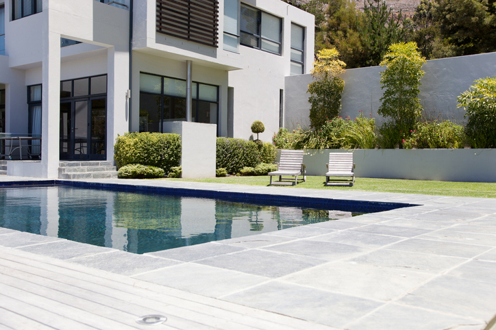 Maison moderne avec une piscine rectangulaire et une terrasse en carrelage gris.