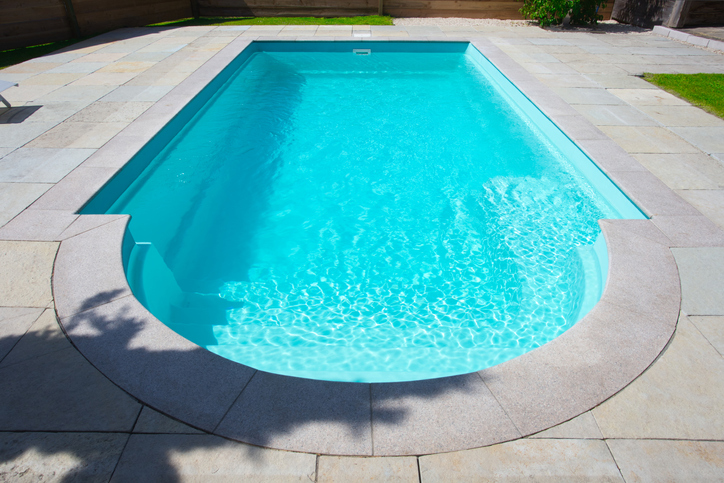 Piscine rectangulaire avec un bord arrondi et terrasse en pierre grise.