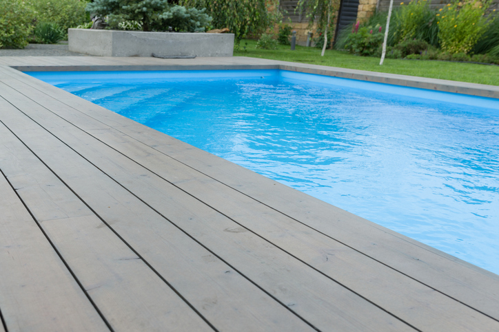 Piscine entourée d'une terrasse en bois gris.