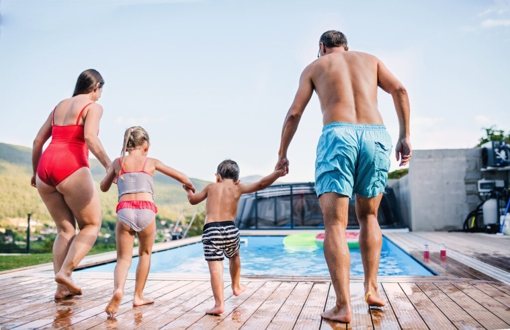 Une famille avec deux enfants sur une terrasse en bois prête à sauter dans une piscine.