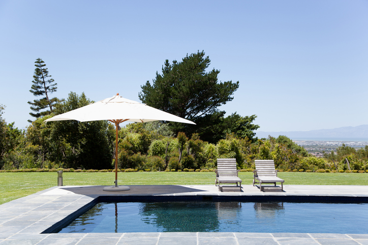 Deux chaises longues sous un parasol au bord d'une piscine avec terrasse en pierre.